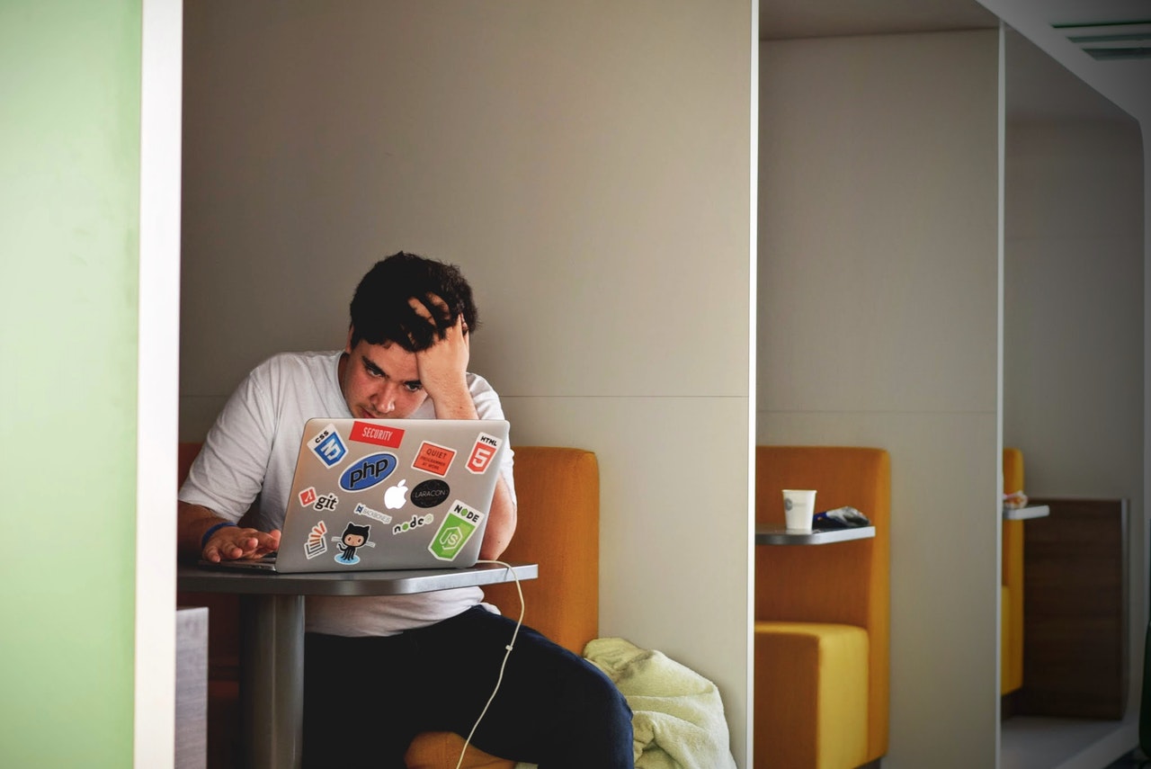 A man runs his hand through his hair in frustration while staring at his laptop